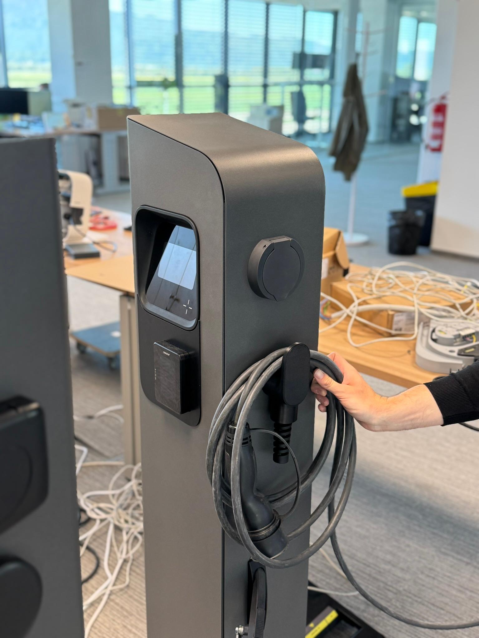 A hand coiling the charging cable onto the holder of a pedestal charger prototype in the office
