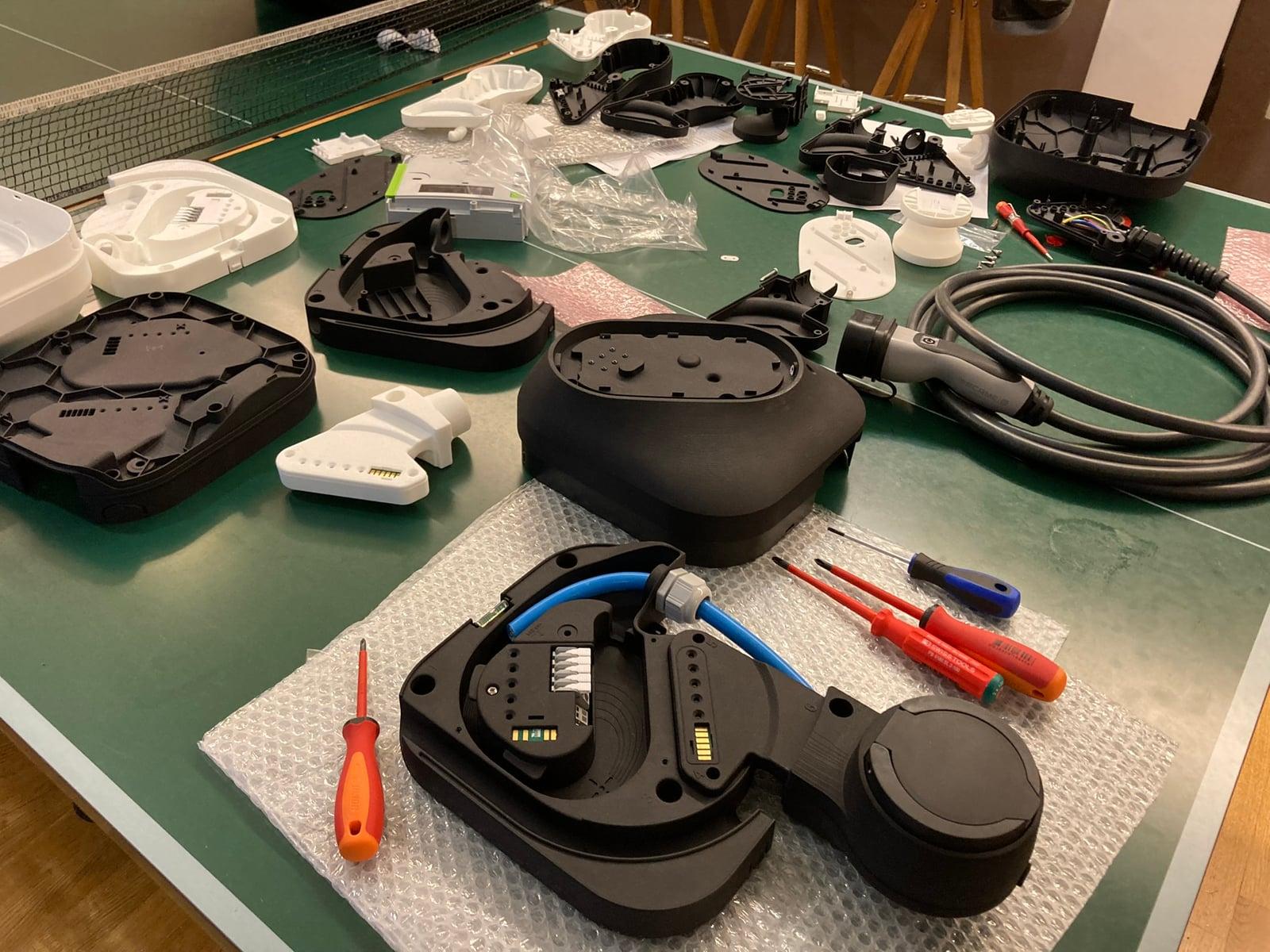 Disassembled charger prototype parts, cables and screwdrivers spread out on a table
