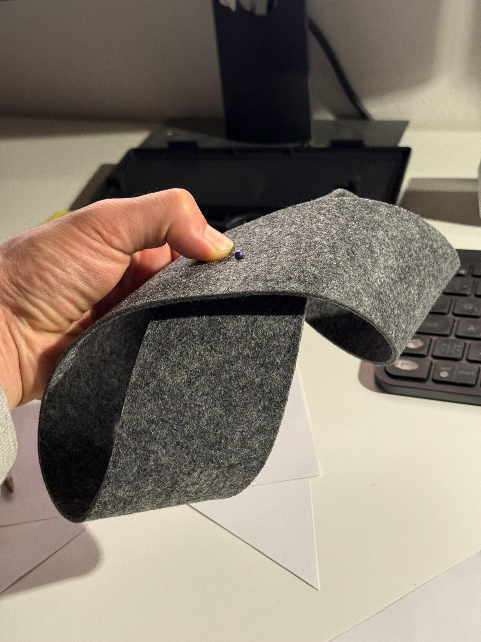 A hand holding a folded grey felt mockup of the lamp shade above a keyboard