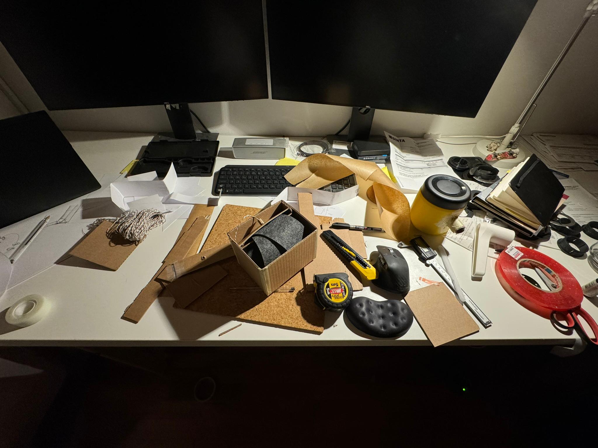 Workshop desk covered with cardboard and felt prototype parts, tools and a tape measure