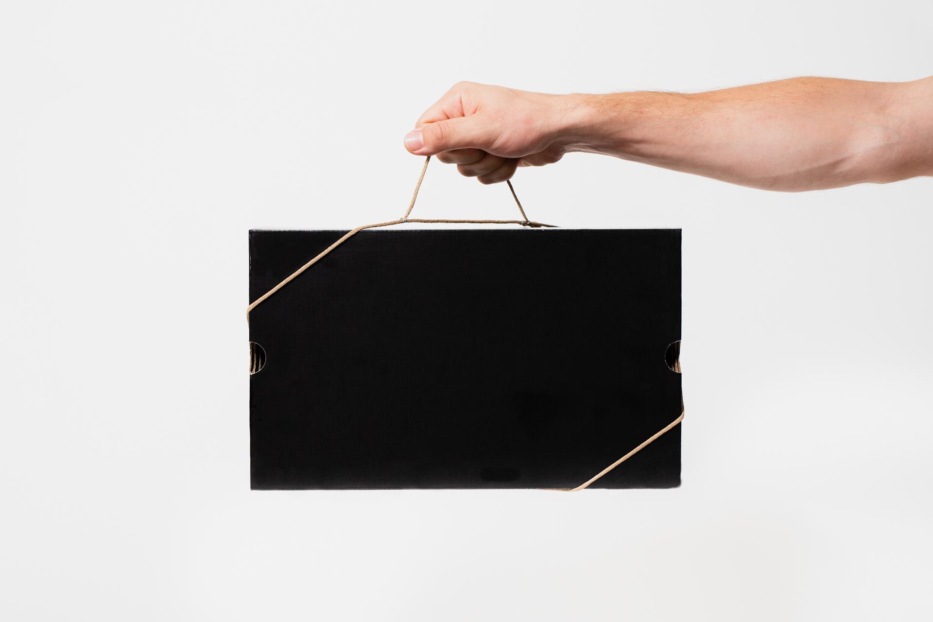 Hand holding a black shoebox by the Bagless Cord