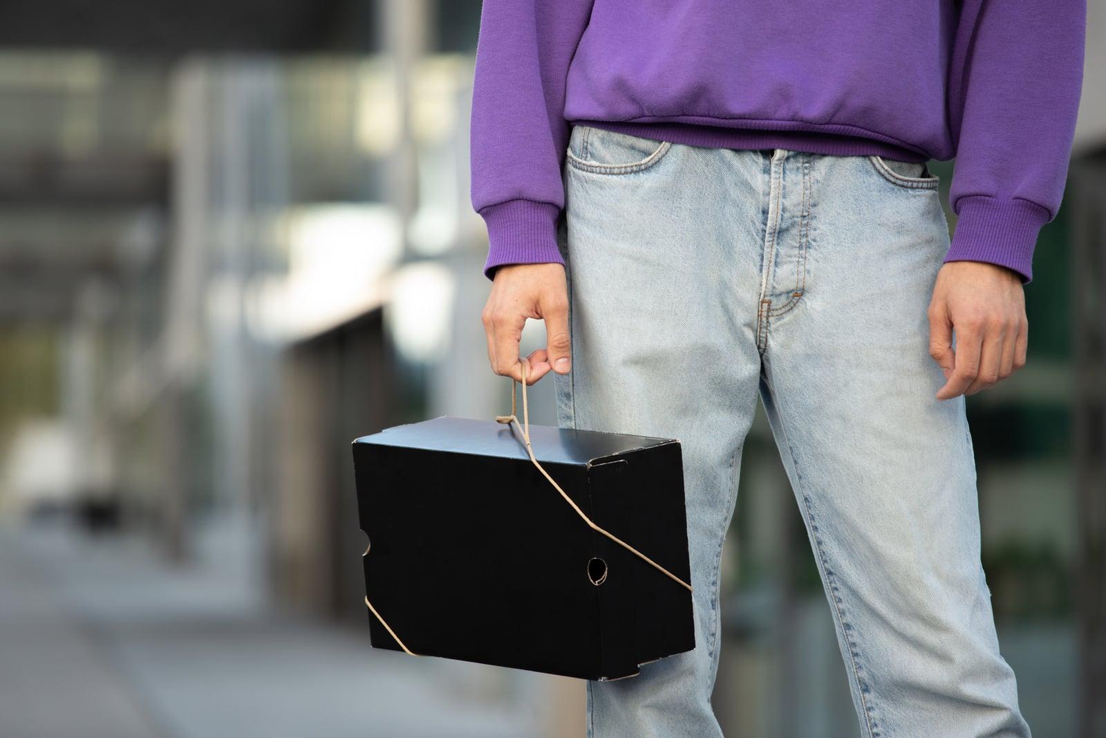 Person carrying a black shoebox with a Bagless Cord on the street