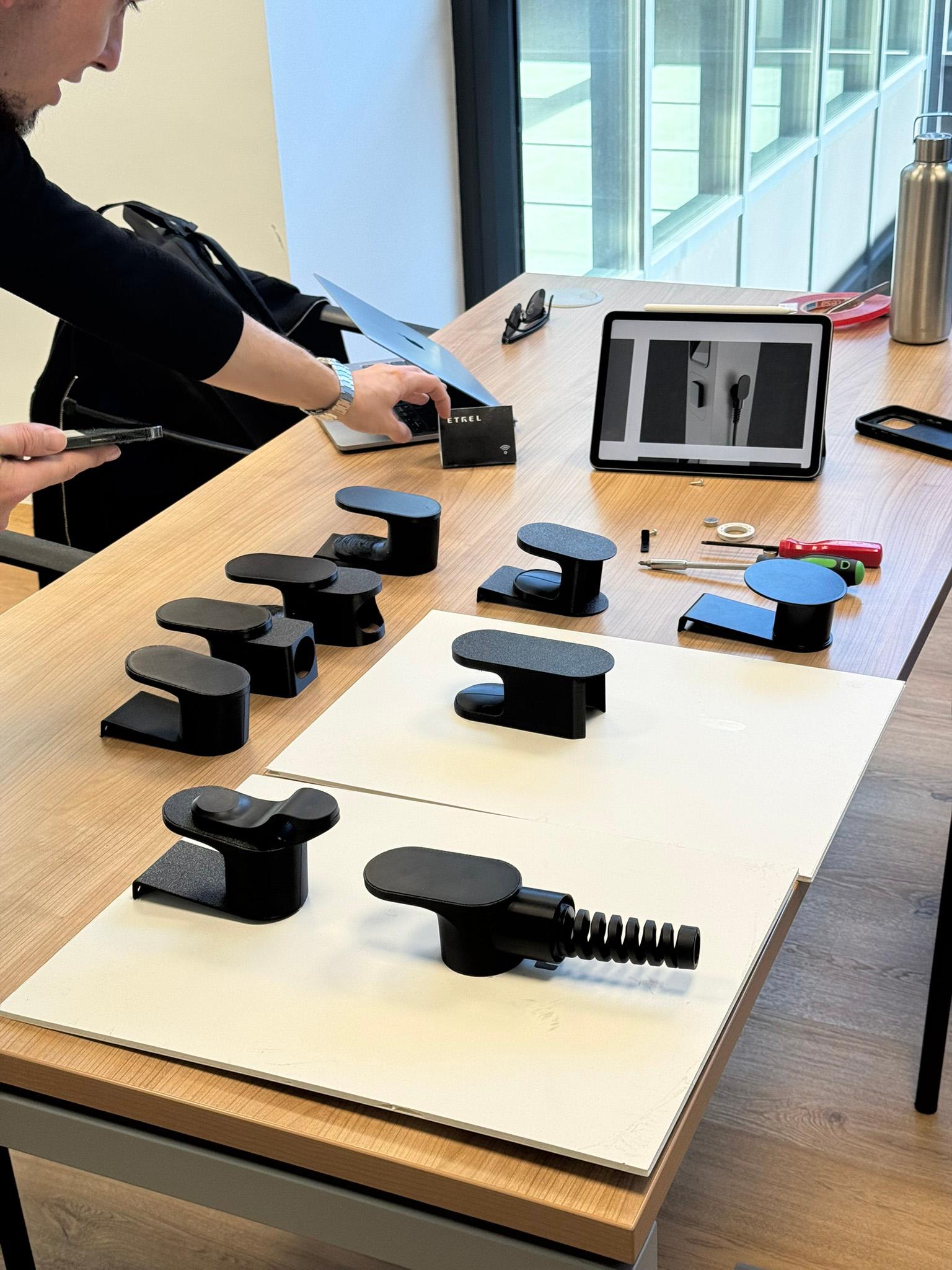 Physical mockups of cable holder variants laid out on a desk during a design review