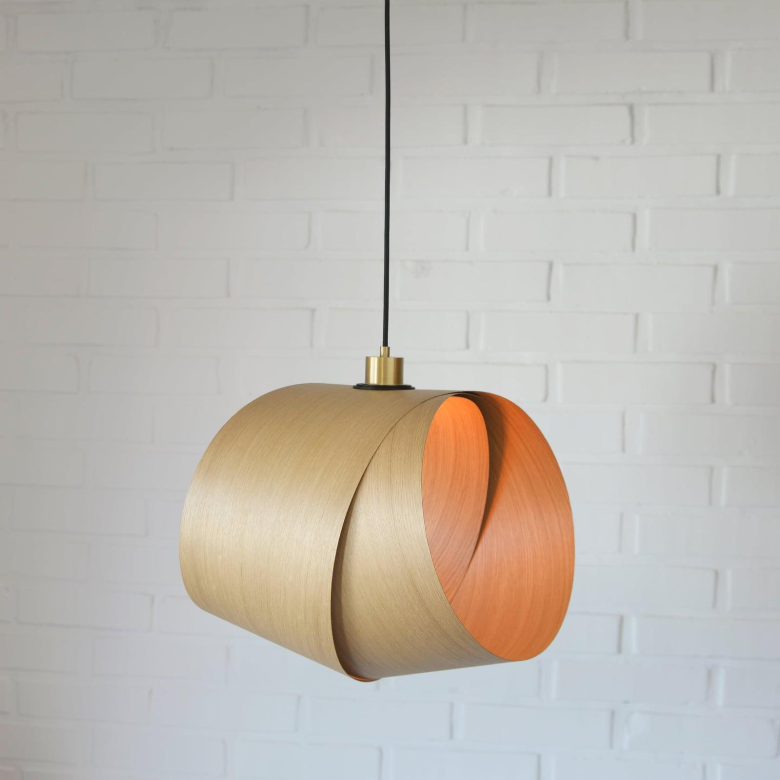 Foldia lamp in oak veneer closed into a rounded shape, unlit, in front of a white brick wall