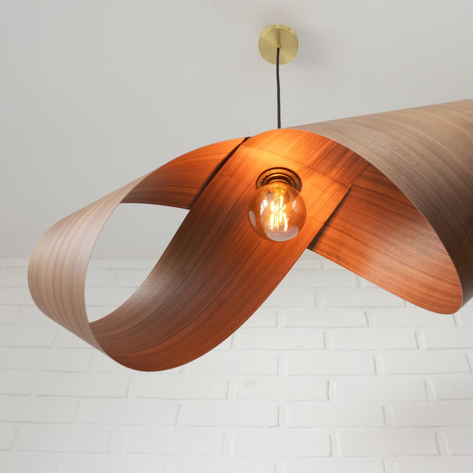 Foldia lamp in walnut veneer, open, with the filament bulb visible, in front of a white brick wall