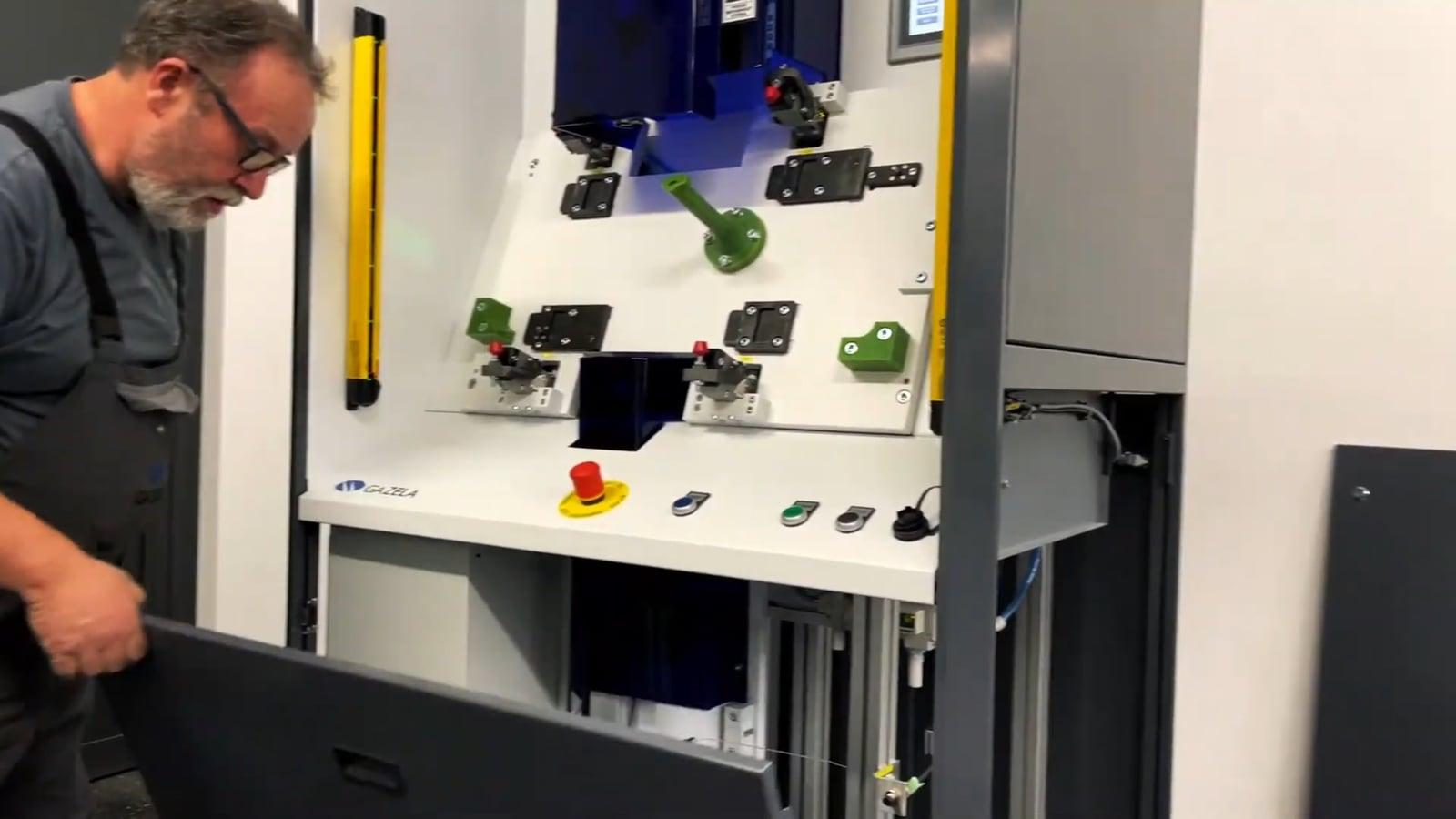 An operator in work overalls looks into the measurement booth working area with green fixtures and control buttons