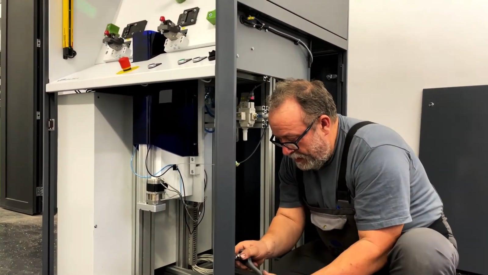 A technician kneels at the open side of the measurement booth working on its internals
