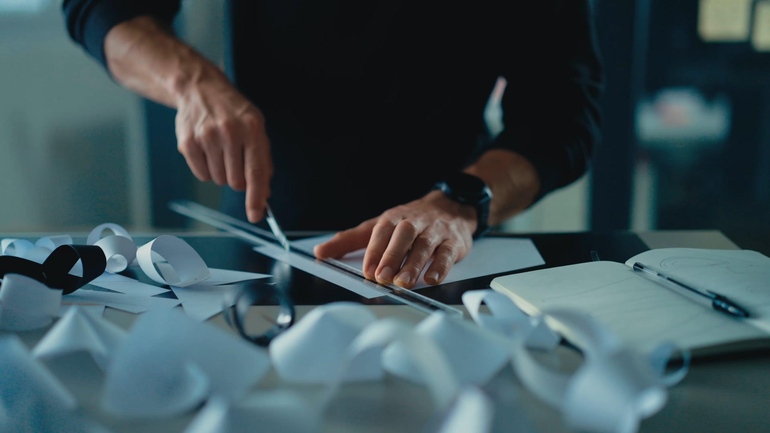 Hands cutting a strip of paper with scissors among paper mockups on a desk