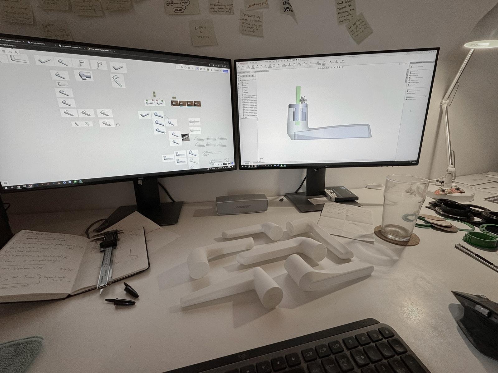 Desk with CAD models of the handle on two screens and white 3D-printed handle models